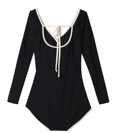 Woman wearing a black long-sleeve one-piece swimsuit with a wrap-style V-neck and light cream trim. - Image 19