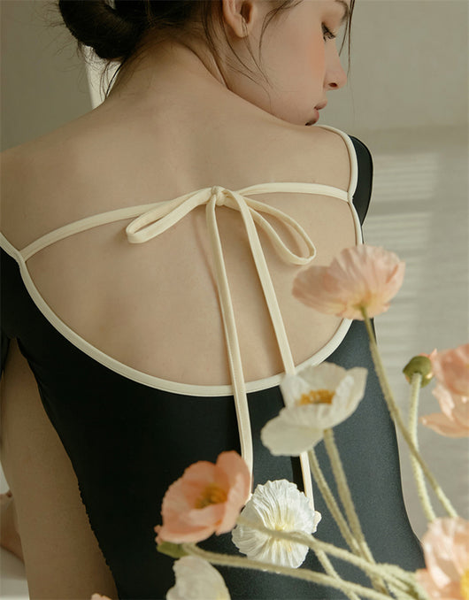 Woman wearing a black long-sleeve one-piece swimsuit with a wrap-style V-neck and light cream trim. - Image 20