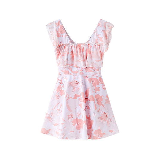 Women's pink and white floral one-piece swimsuit with ruffled cap sleeves and a skirted bottom, shown on a model by the ocean. - Image 17