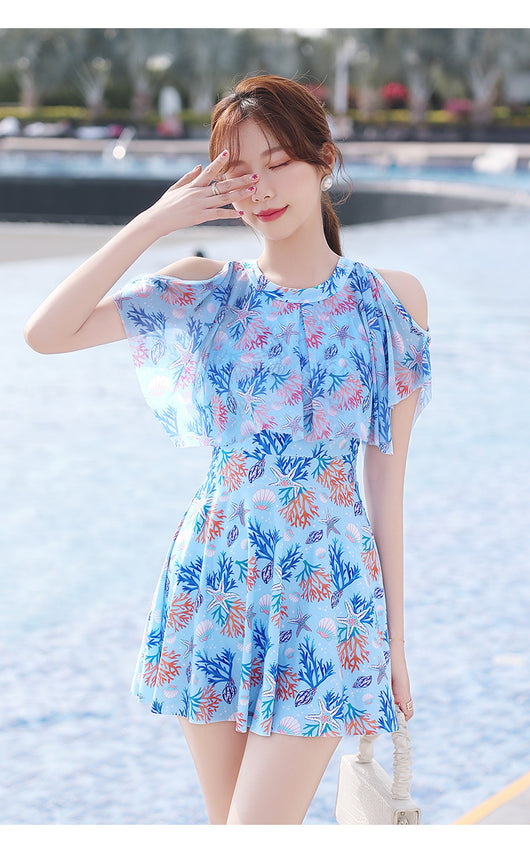 Pink dress-style swimsuit with cold-shoulder ruffles and a vibrant coral and seashell print, modeled by a woman. - Image 17