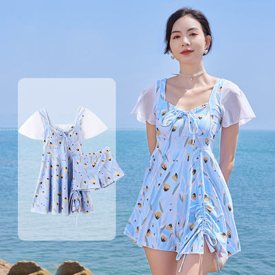 Woman in a light blue floral print swimsuit with sheer white short sleeves and a skirted bottom at the beach. - Image 14