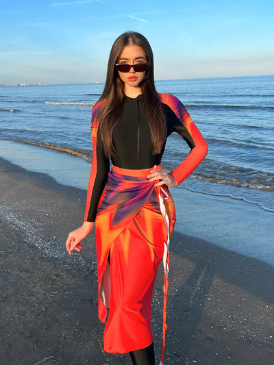 Woman in a black long-sleeve rash guard, black swim leggings, and a vibrant tie-dye sarong on a sunny beach. - Image 10