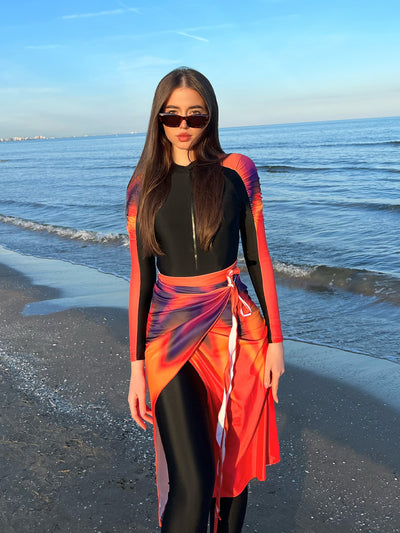 Woman in a black long-sleeve rash guard, black swim leggings, and a vibrant tie-dye sarong on a sunny beach. - Image 11
