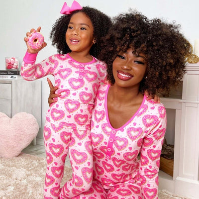 Mother and daughter in matching black and pink heart-print long-sleeve pajamas, smiling and holding small pink hearts. - Image 6