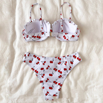 Women's white bikini swimsuit with red cherry print, featuring a ruffled top and high-cut bottom, modeled by a pool. - Image 11