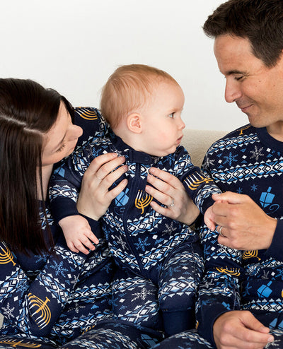 Family of five wearing matching navy blue Hanukkah pajamas with gold menorahs, blue dreidels, and white snowflakes.