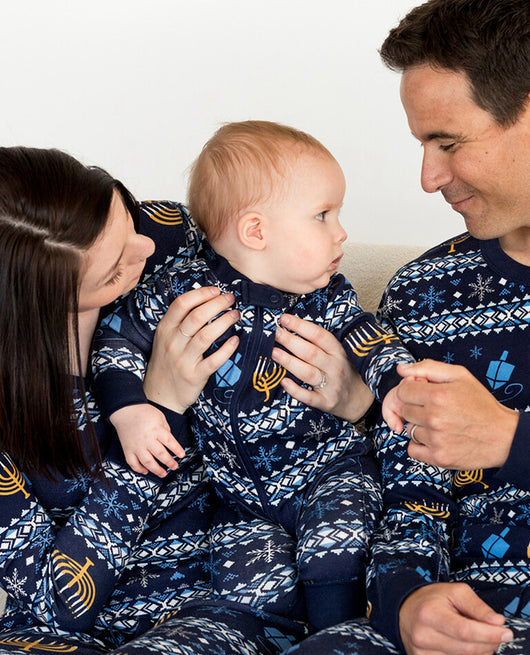 Family of five wearing matching navy blue Hanukkah pajamas with gold menorahs, blue dreidels, and white snowflakes.