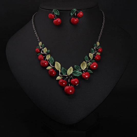 Cherry necklace and earring set featuring red enamel cherries and green leaves on a dark chain, displayed on a black bust.