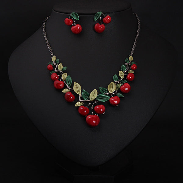 Cherry necklace and earring set featuring red enamel cherries and green leaves on a dark chain, displayed on a black bust.
