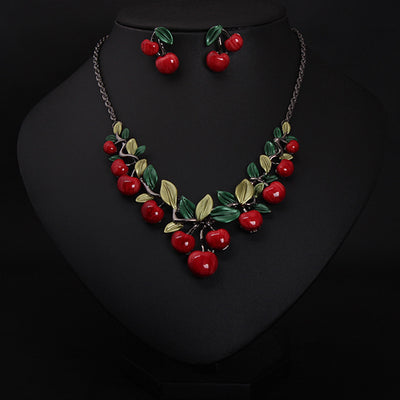 Cherry necklace and earring set featuring red enamel cherries and green leaves on a dark chain, displayed on a black bust.