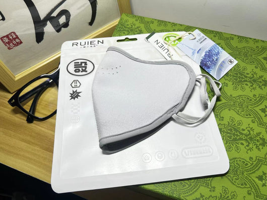 Dark gray cotton head-mounted mask with adjustable ear loops, shown in packaging on a patterned green surface. - Image 13