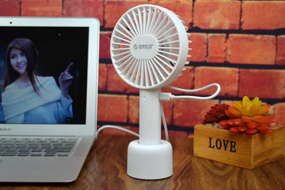 White ORICO FH1 handheld USB fan with charging dock, USB cable, and user manuals on a wooden desk. - Image 6