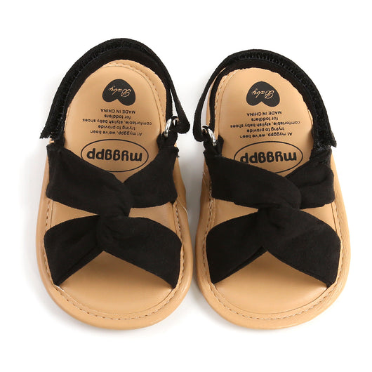 Black baby sandals with knotted cross straps and a matching black floral headband on a white background. - Image 7