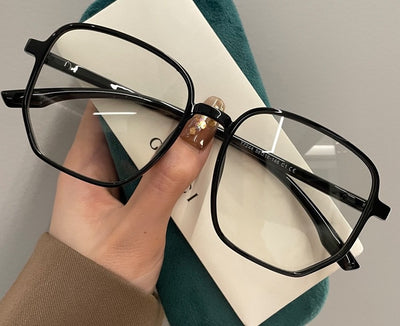Mocha brown irregular frame glasses with clear lenses, held over a dark green velvet glasses case. - Image 15