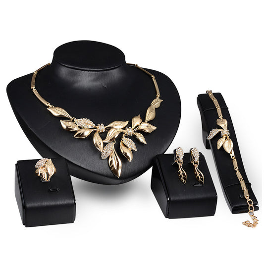 Gold-toned four-piece bridal wedding jewelry set with leaf design and clear rhinestones, including necklace, earrings, bracelet, and ring.