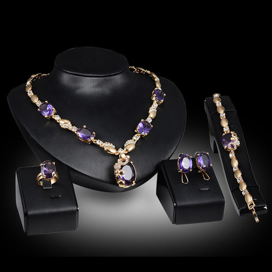 Four-piece gold-toned jewelry set with oval purple gemstones: necklace, ring, earrings, and bracelet.
