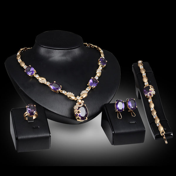 Four-piece gold-toned jewelry set with oval purple gemstones: necklace, ring, earrings, and bracelet.