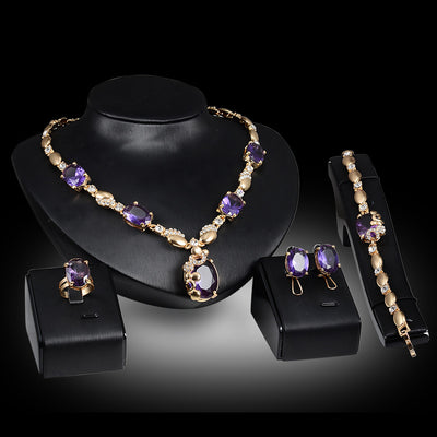 Four-piece gold-toned jewelry set with oval purple gemstones: necklace, ring, earrings, and bracelet.