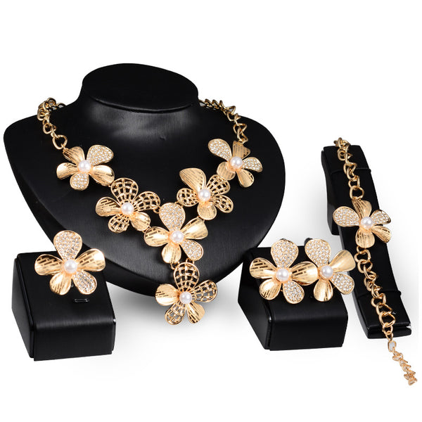 Gold-tone four-piece jewelry set with flower motifs, featuring a necklace, bracelet, ring, and earrings, all with faux pearls and clear rhinestones.