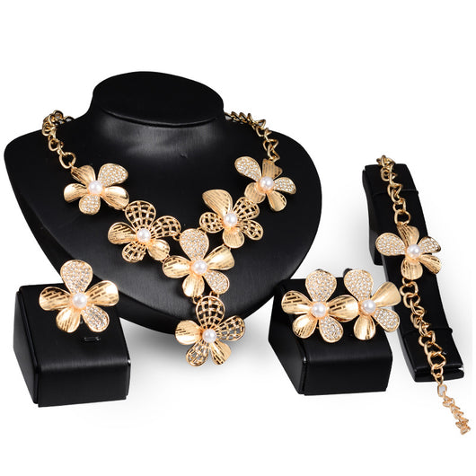 Gold-tone four-piece jewelry set with flower motifs, featuring a necklace, bracelet, ring, and earrings, all with faux pearls and clear rhinestones.