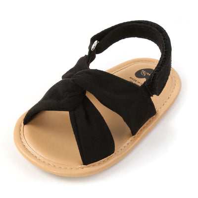 Black baby sandals with knotted cross straps and a matching black floral headband on a white background. - Image 38