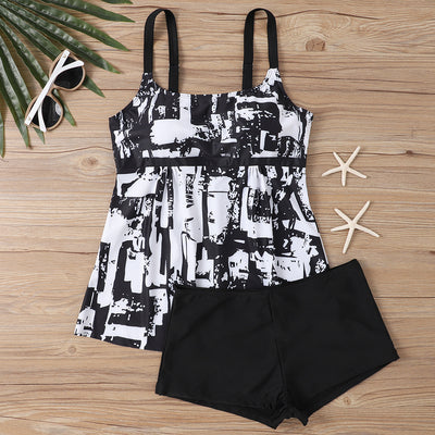 Woman in a black and white abstract print tankini top with black swim shorts on a sunny beach. - Image 17