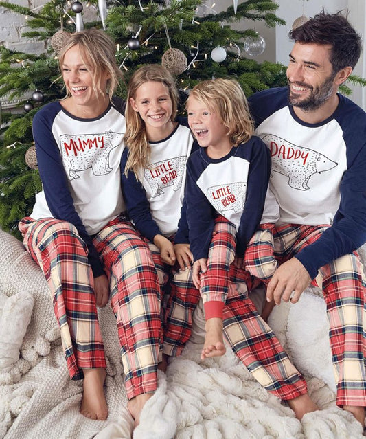 Family of four wearing matching Christmas pajamas with white and navy bear print tops and red plaid pants.