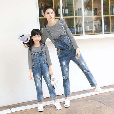 Mother and daughter wearing matching distressed denim overalls over black and white striped long-sleeve shirts.
