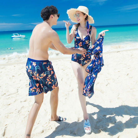 Man wearing navy blue swim shorts with a vibrant orange and green floral pattern, standing on a sunny beach. - Image 3