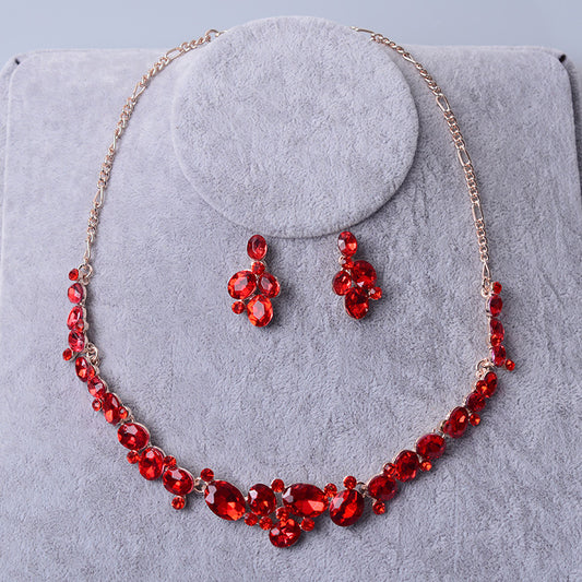 Silver-tone bridal necklace and matching drop earrings set with clear oval and round rhinestones, displayed on a gray velvet stand.
