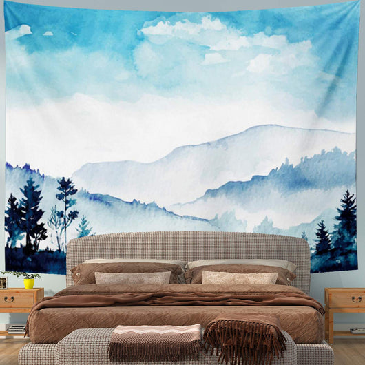 Blue watercolor landscape tapestry with mountains, trees, and a cloudy sky, hanging above a bed.