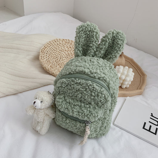 Pink fuzzy mini backpack with bear ears and a small white teddy bear keychain on a white bed. - Image 13