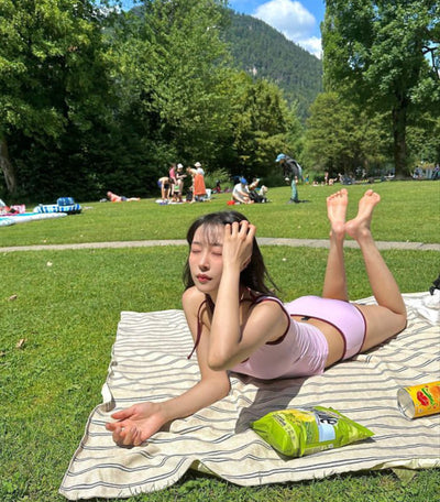 Women's light purple one-shoulder swimsuit with dark red contrast trim, lying on a striped blanket on green grass. - Image 8