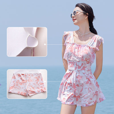 Women's pink and white floral one-piece swimsuit with ruffled cap sleeves and a skirted bottom, shown on a model by the ocean. - Image 9