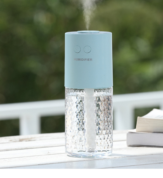 Dark blue and clear portable humidifier with a textured water tank on a white desk next to a laptop. - Image 9