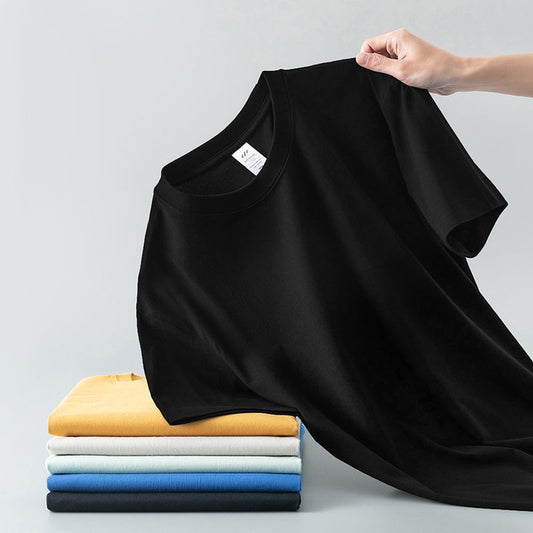 Light gray short-sleeve t-shirt with a round neck, held up to show its smooth fabric. A stack of folded t-shirts in various colors is visible in the background. - Image 2