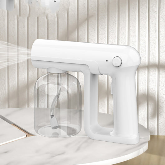 Black wireless alcohol blue light disinfection spray gun with clear reservoir, actively misting, on a marble surface. - Image 15