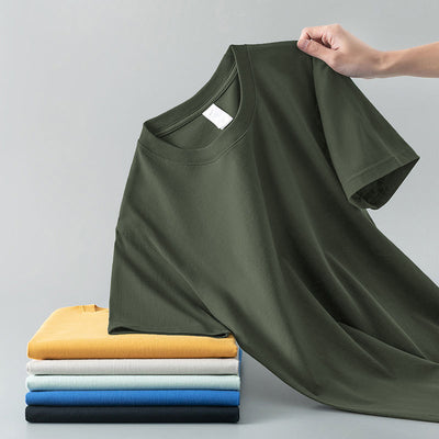 Light gray short-sleeve t-shirt with a round neck, held up to show its smooth fabric. A stack of folded t-shirts in various colors is visible in the background. - Image 9