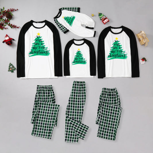 Matching family Christmas pajamas with white and black raglan tops featuring a green Christmas tree graphic and plaid pants.