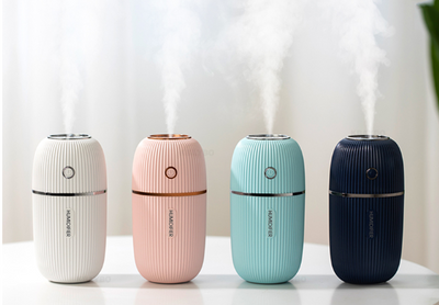 Pink mini ultrasonic air humidifier with ribbed texture and rose gold accents, emitting a fine mist on a white shelf. - Image 3