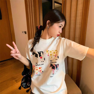 White loose-fit short-sleeve top with colorful retro cartoon cow print, modeled by a woman with plaid pants. - Image 10