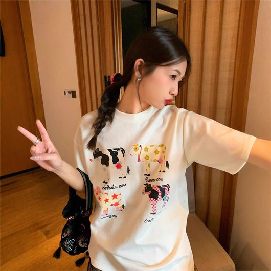 White loose-fit short-sleeve top with colorful retro cartoon cow print, modeled by a woman with plaid pants. - Image 10