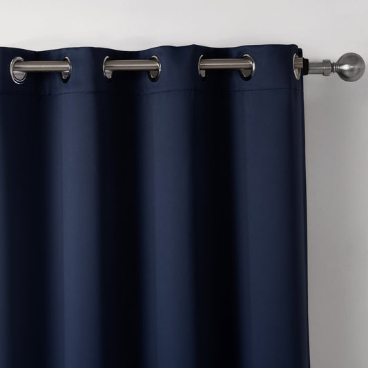 Dark blue blackout curtains with silver grommet tops hanging on a rod in a modern bedroom setting.