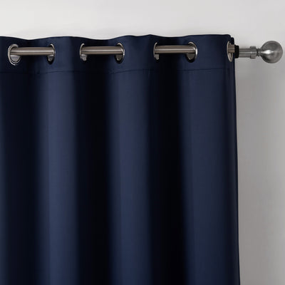 Dark blue blackout curtains with silver grommet tops hanging on a rod in a modern bedroom setting.