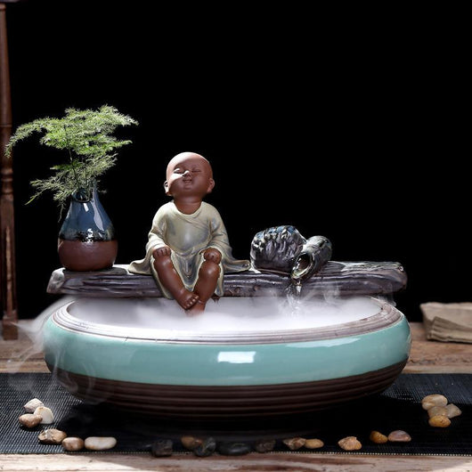 Ceramic flowing water ornament with a meditating monk figurine, small plant, and misting humidifier in a teal and brown bowl. - Image 4