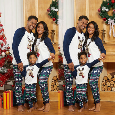 Family of three wearing matching Christmas pajamas with reindeer tops and snowflake-patterned pants.