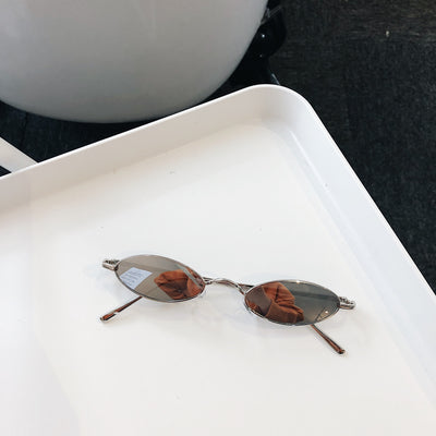 Silver-framed oval sunglasses with dark lenses reflecting a warm-toned object, displayed on a white tray. - Image 5