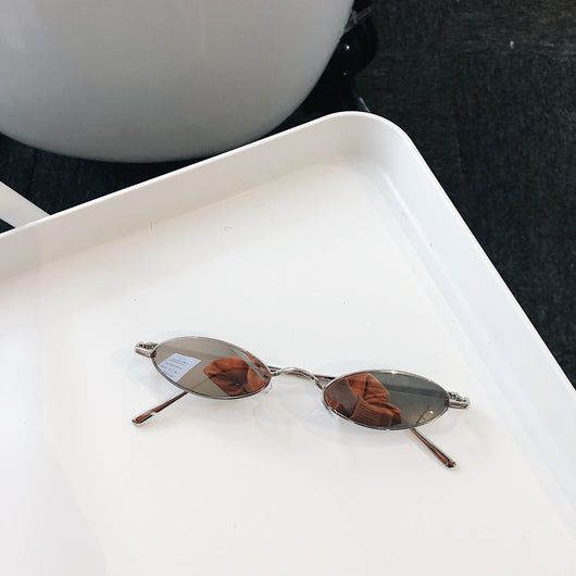 Silver-framed oval sunglasses with dark lenses reflecting a warm-toned object, displayed on a white tray. - Image 5