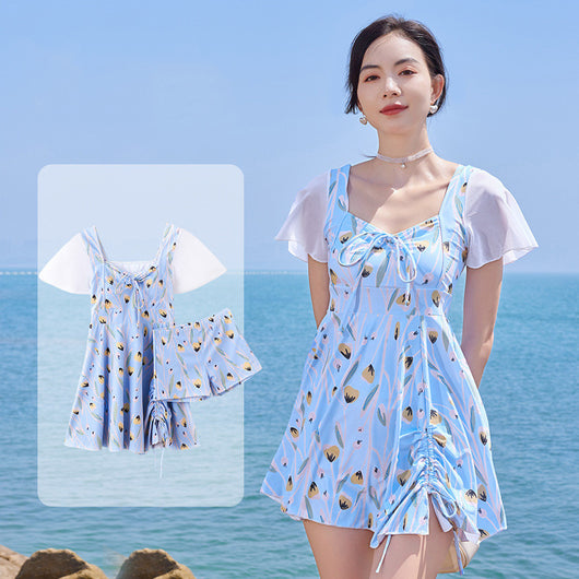 Woman in a light blue floral print swimsuit with sheer white short sleeves and a skirted bottom at the beach. - Image 8