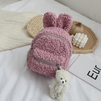Pink fuzzy mini backpack with bear ears and a small white teddy bear keychain on a white bed. - Image 7